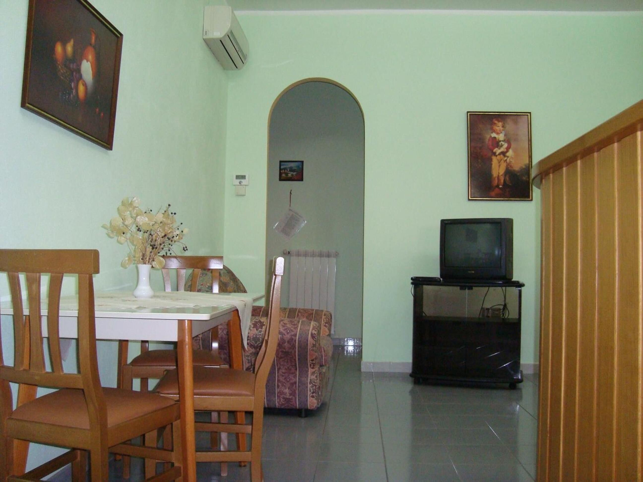 A dining area with a table and chairs, a sofa, a television on a stand, and a radiator.