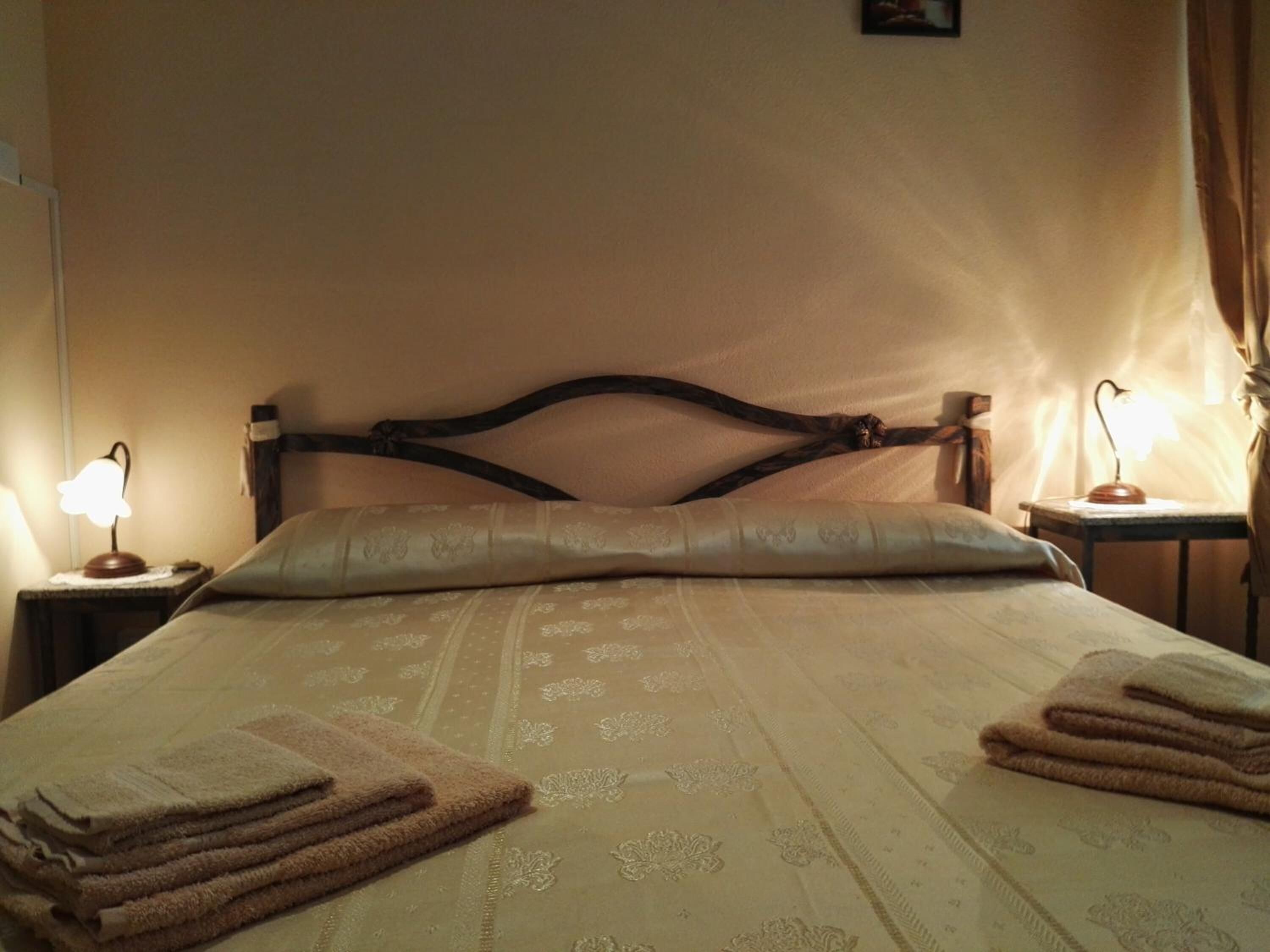 A neatly made bed with a patterned bedspread, two bedside lamps, and folded towels on the bed.