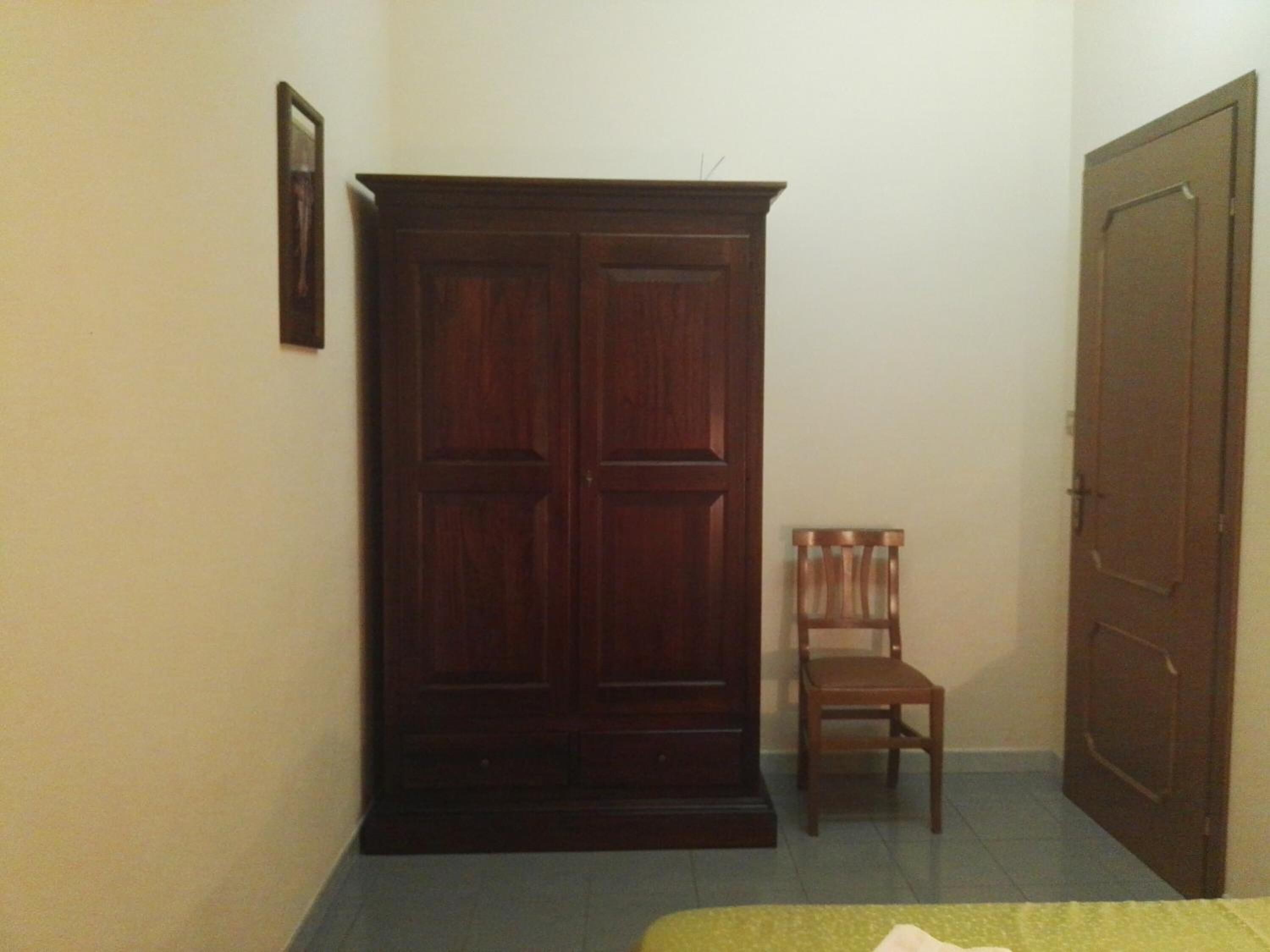 A room with a wooden wardrobe, a chair, and a door.