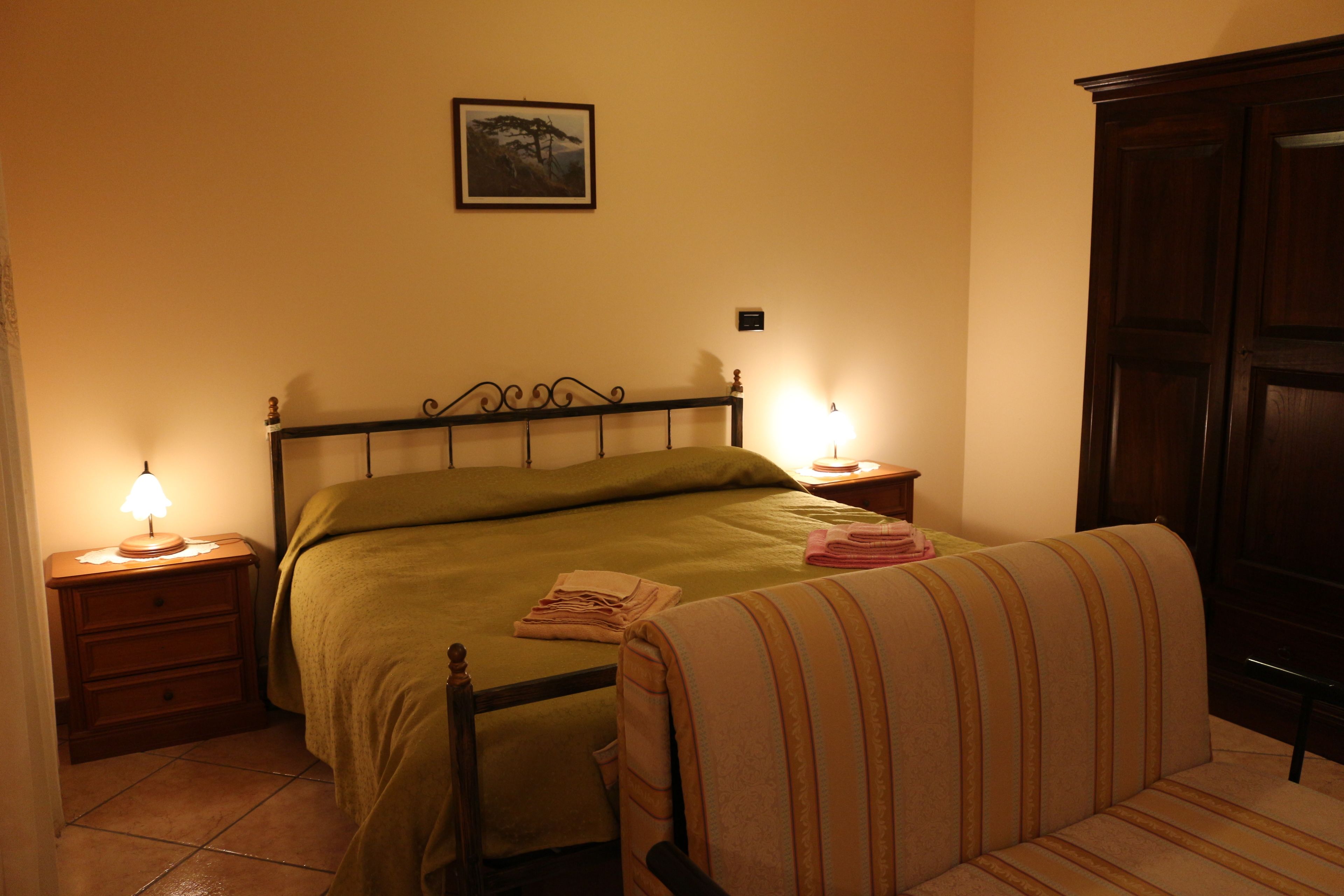 Ein Schlafzimmer mit einem Bett, einem Nachttisch mit Lampe, einem Sessel und einem Kleiderschrank.