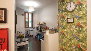 Cozinha compacta com área de jantar, um relógio na parede e papel de parede com motivos tropicais.