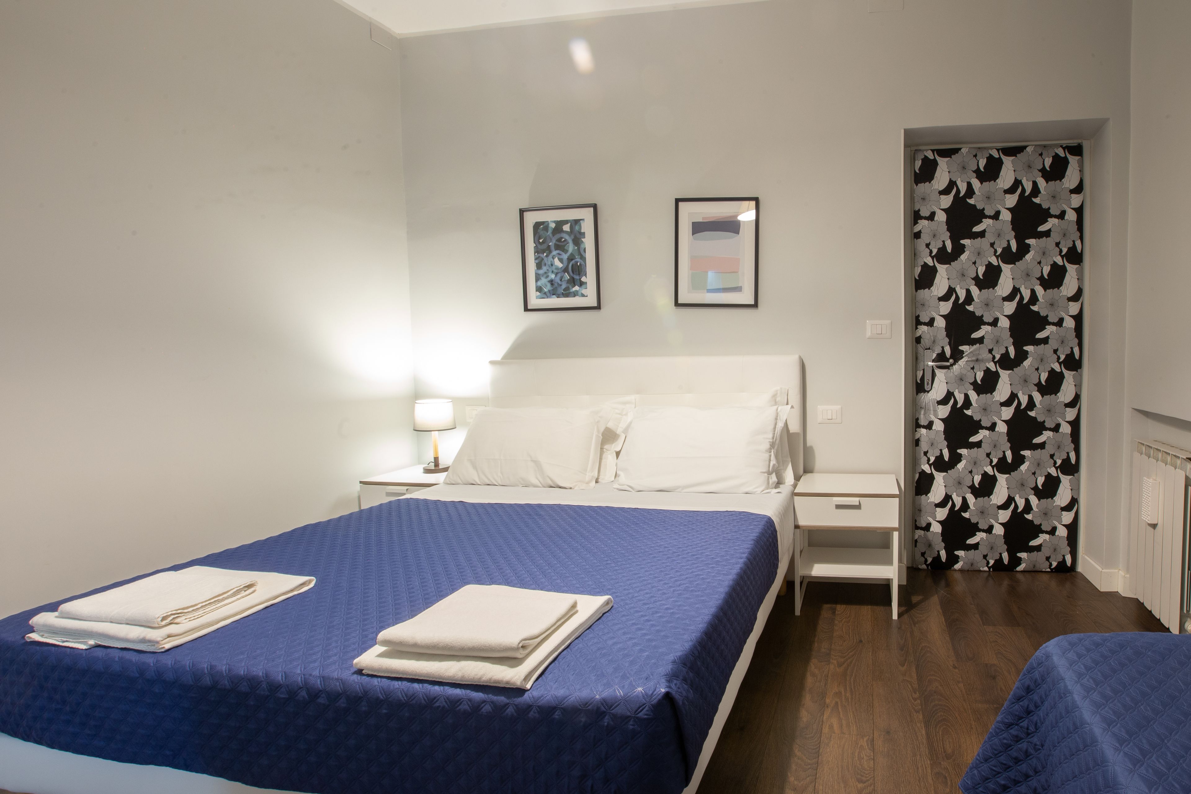 Quarto de hotel com uma cama grande, mesa de cabeceira e porta com cortina floral.