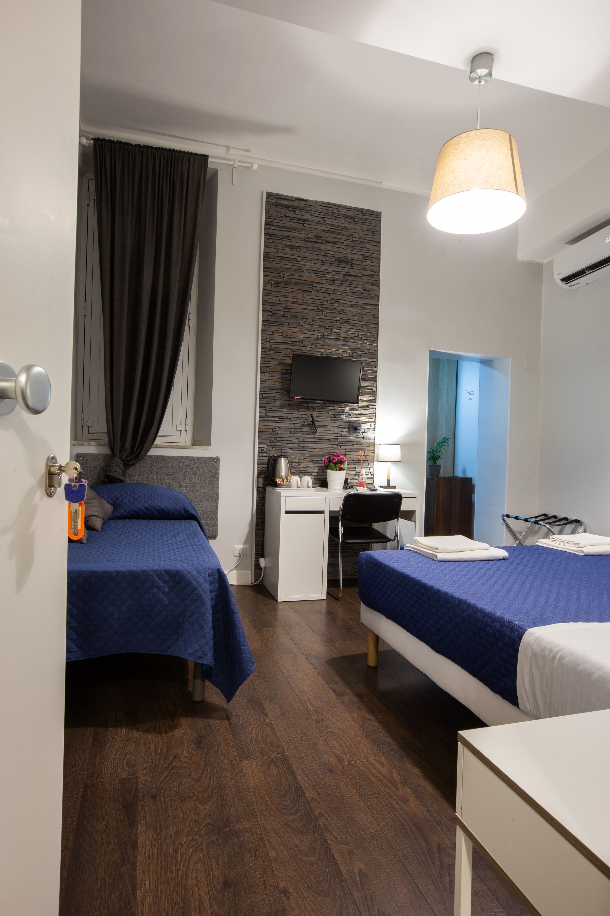 A hotel room with two beds, a desk, a chair, a TV, and a window with curtains.