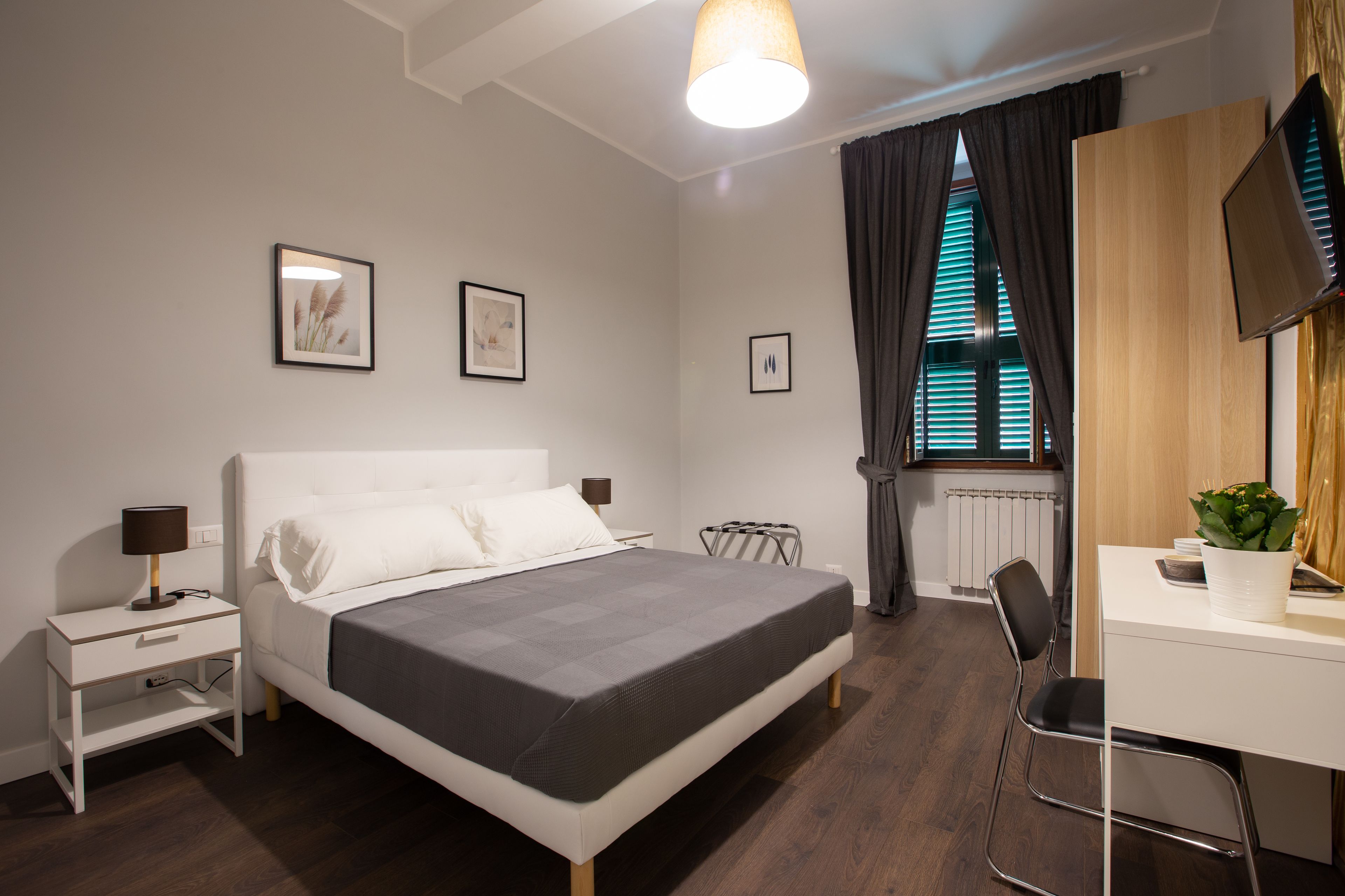 A modern bedroom with a bed, bedside tables, a desk, a chair, and a TV.