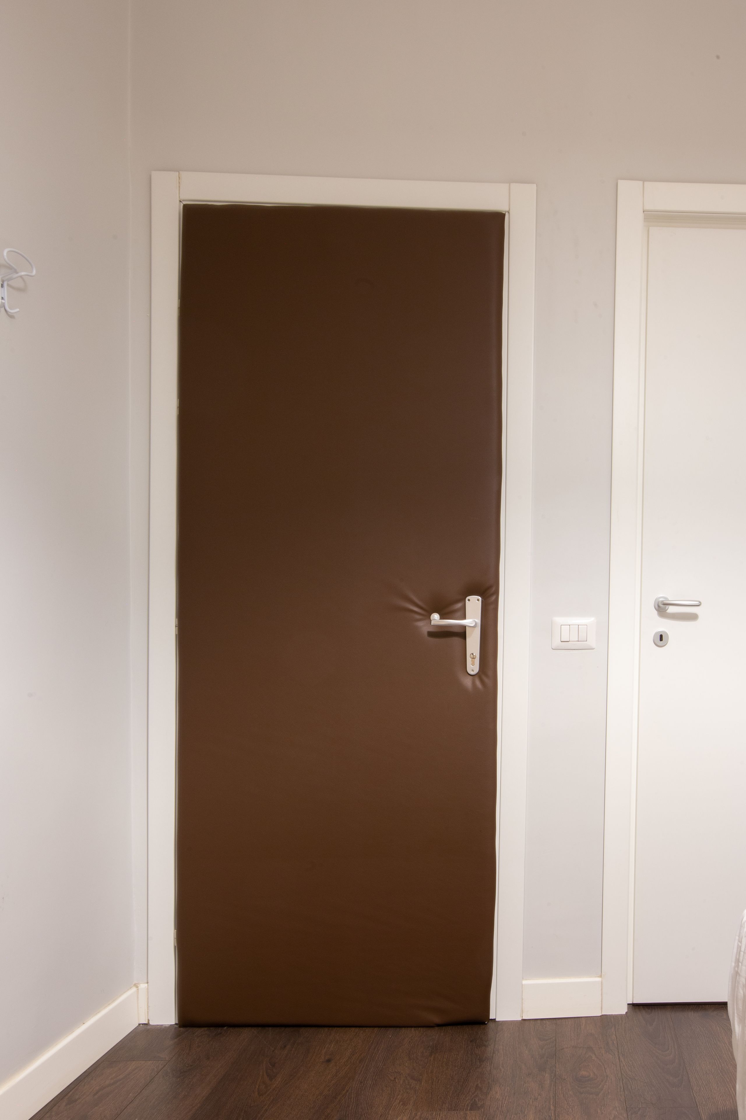 Una porta chiusa con maniglia, un interruttore della luce e una serratura sulla parete adiacente.
