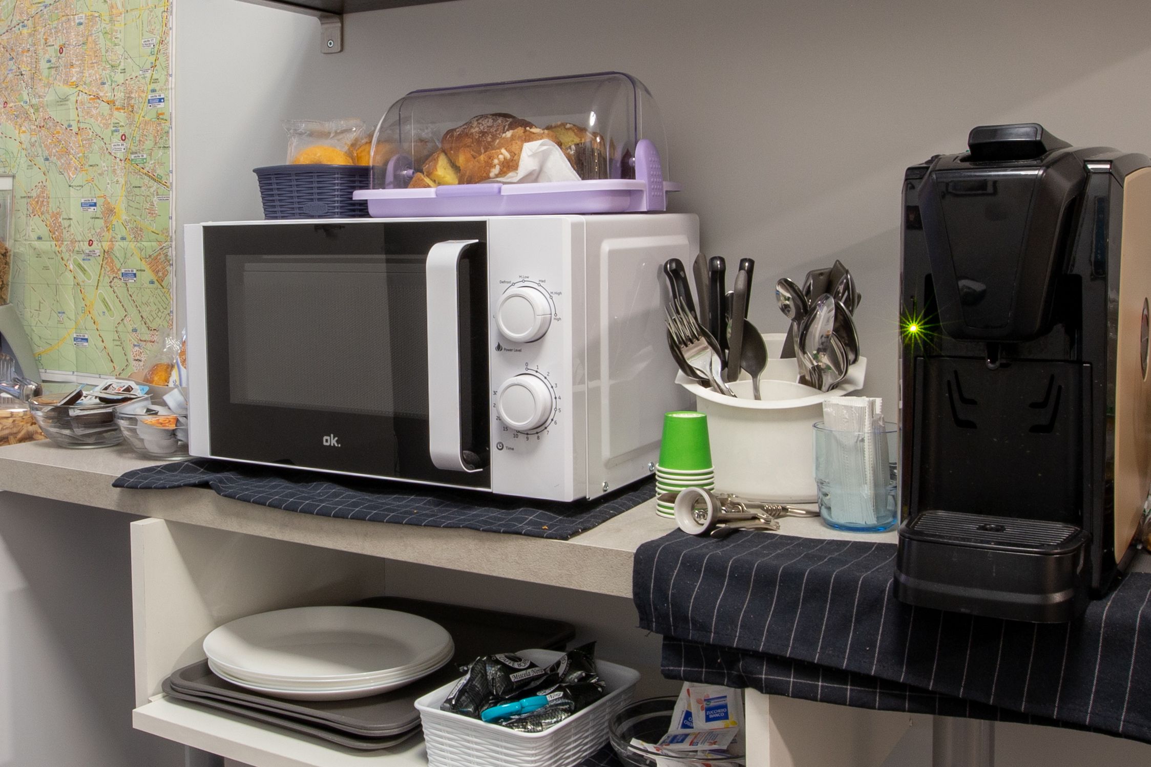 Una kitchenette equipada con microondas, tostadora y cafetera. En la encimera, hay platos, tazas y cubiertos.