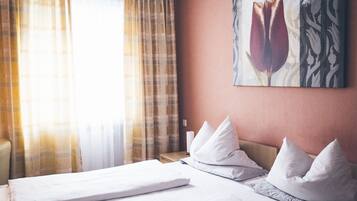 Ein Hotelzimmer mit Bett, weißen Kissen, einem Wandbild mit Tulpen und einem Vorhangfenster.