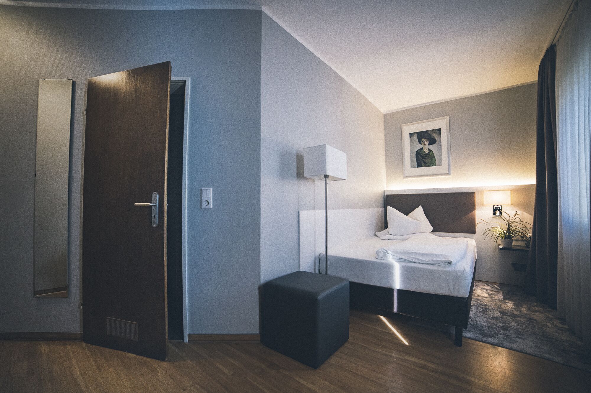 A hotel room with a bed, bedside table, lamp, and a door.
