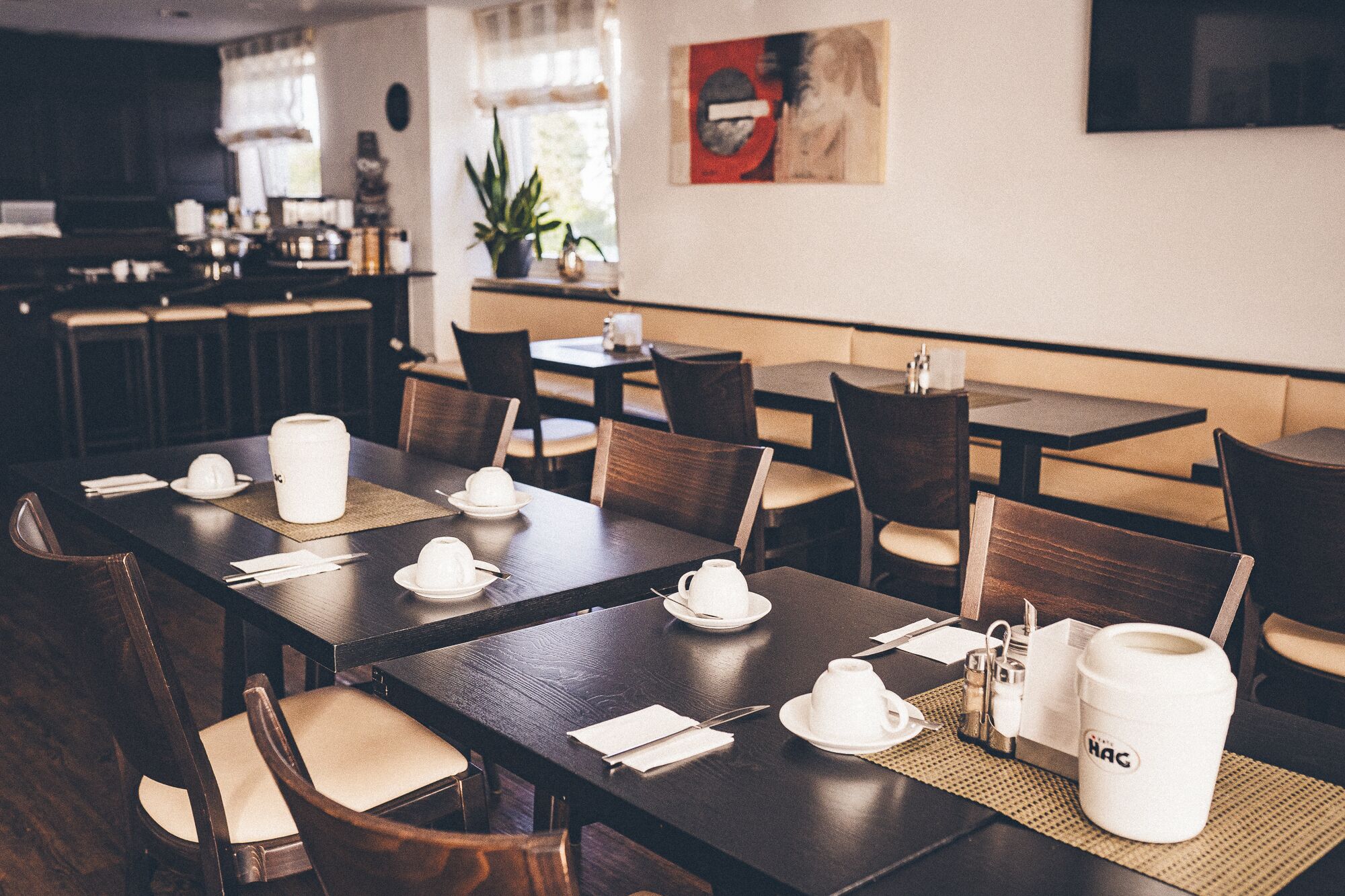 Een restaurant met houten tafels en stoelen, wit servies en een koffiemok op tafel.