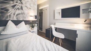 A modern hotel room with a bed, a desk, a chair, a potted plant, and a large abstract artwork on the wall. - Gartenstadt Hotel (Ludwigshafen)
