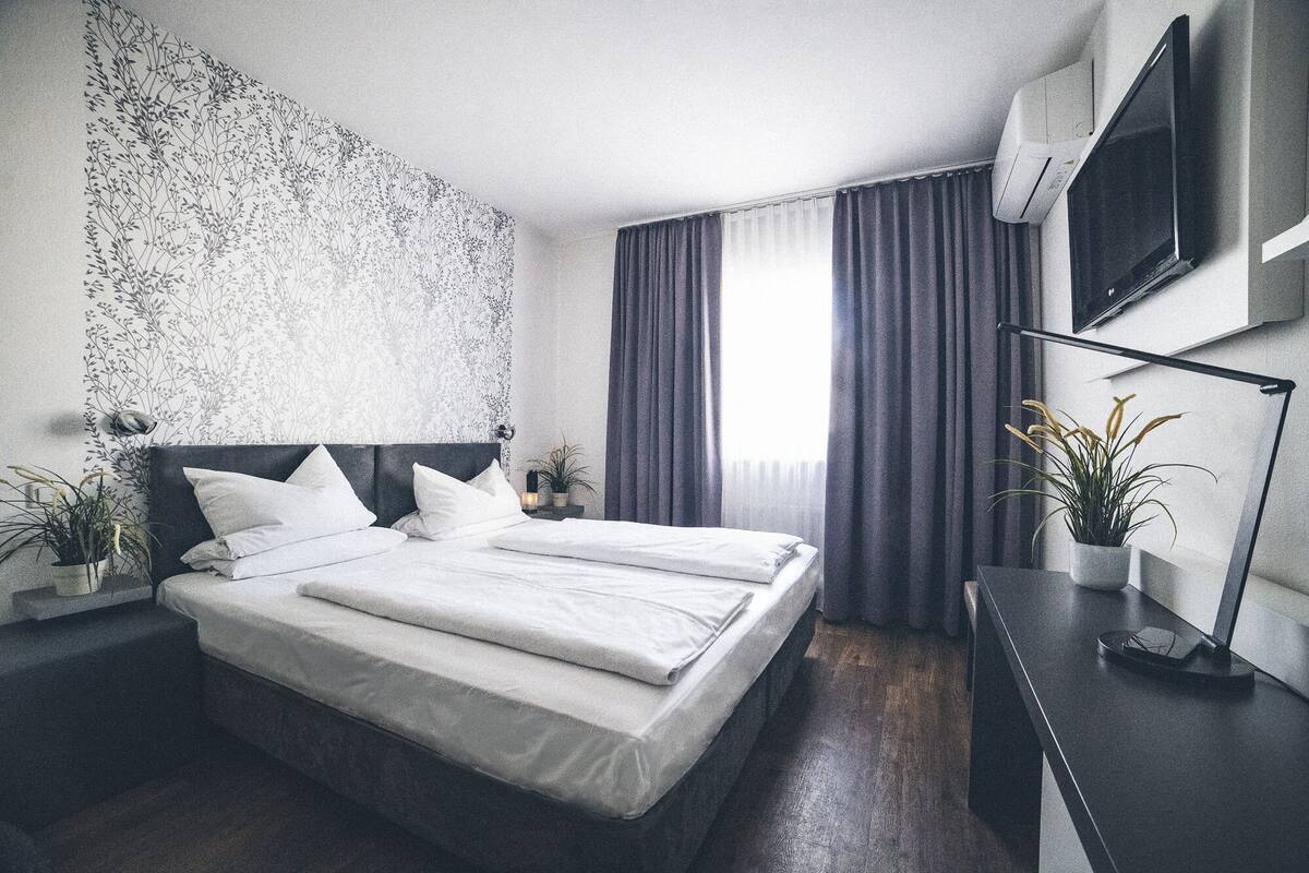 A modern hotel room with a large bed, a flat-screen TV, and a view of the city.