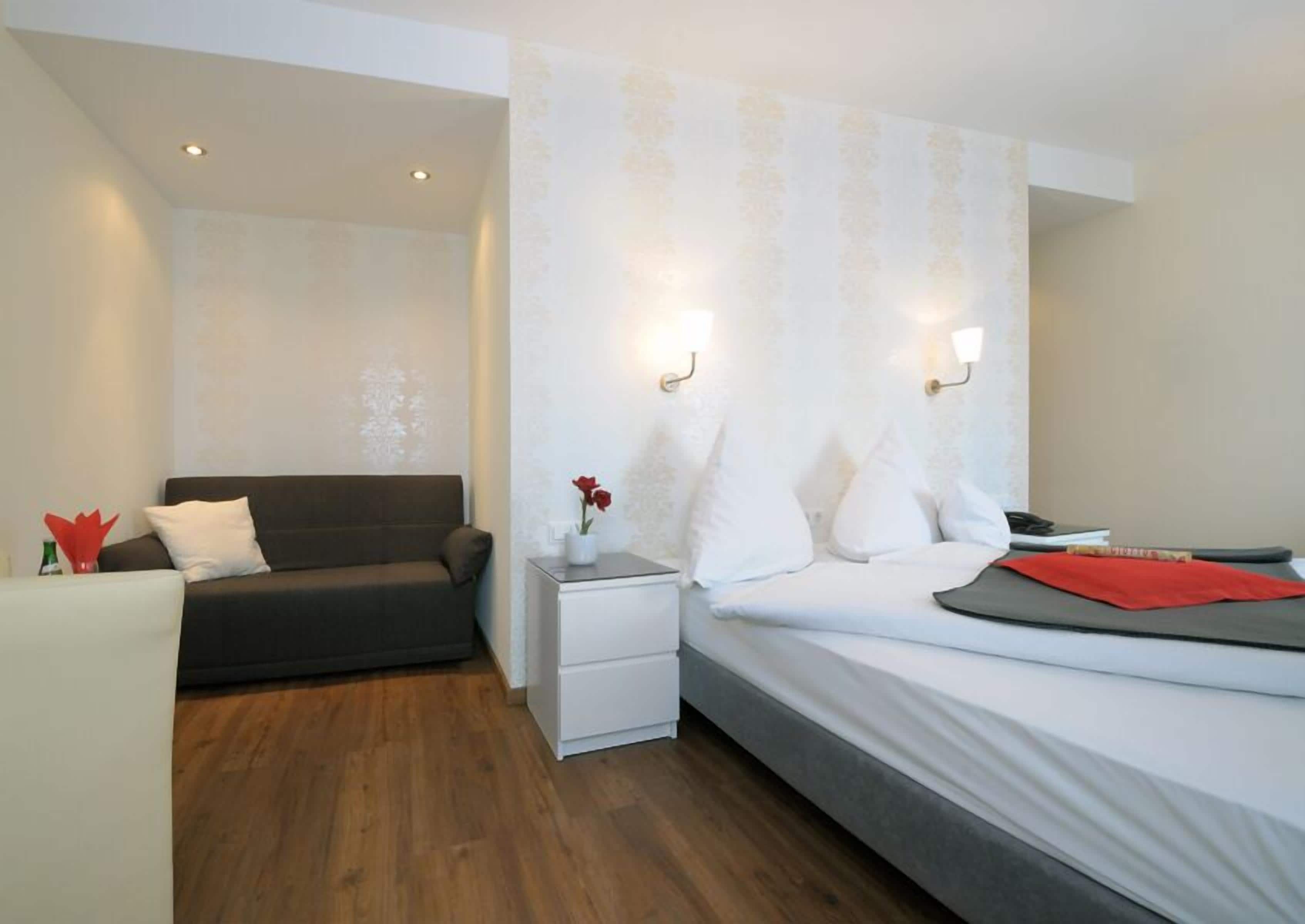 A hotel room with a bed, a sofa, a nightstand, and a small table with a vase of flowers.