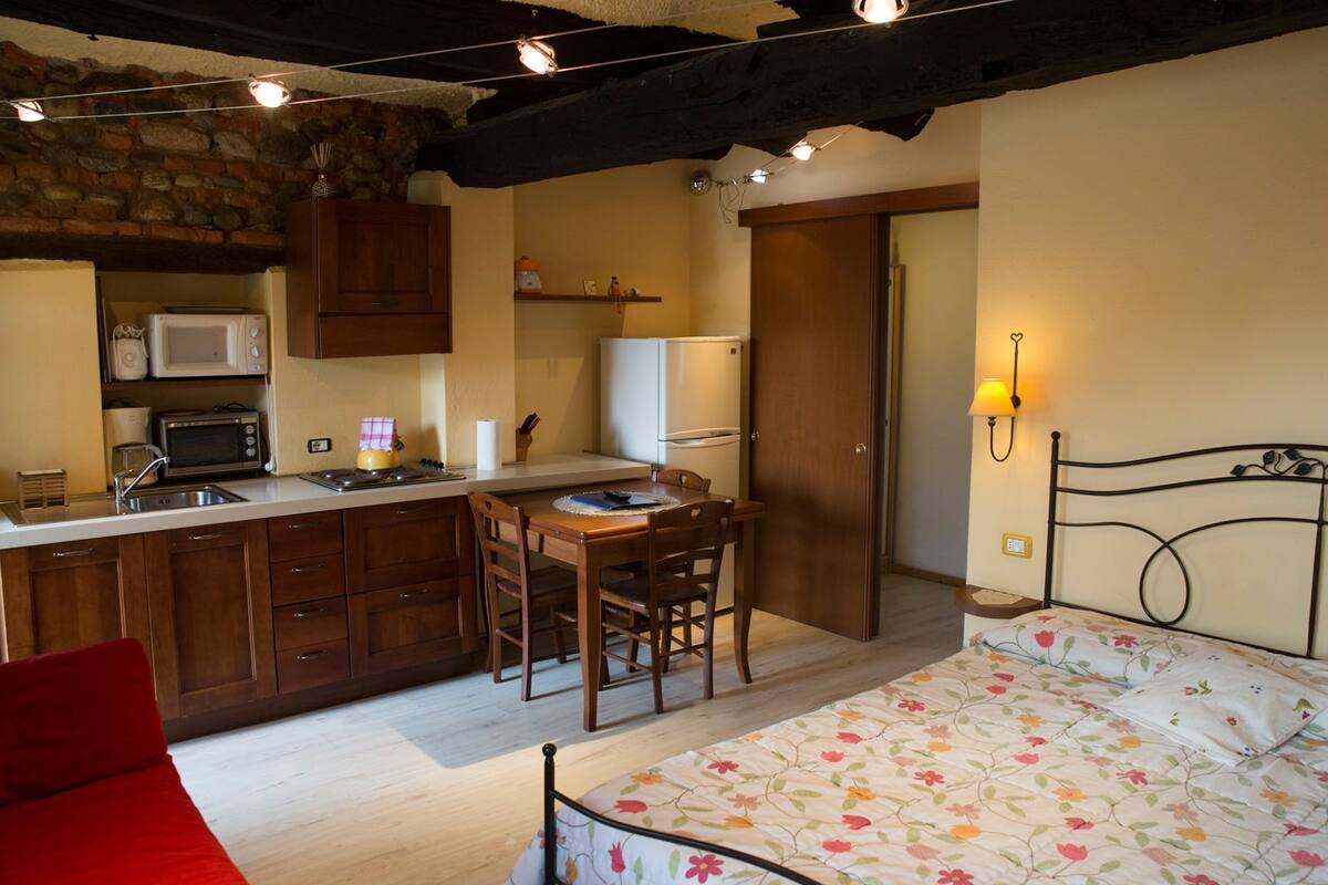 Una cocina compacta con microondas, estufa y lavamanos, un pequeño comedor con mesa y sillas, y una cama con ropa de cama estampada.