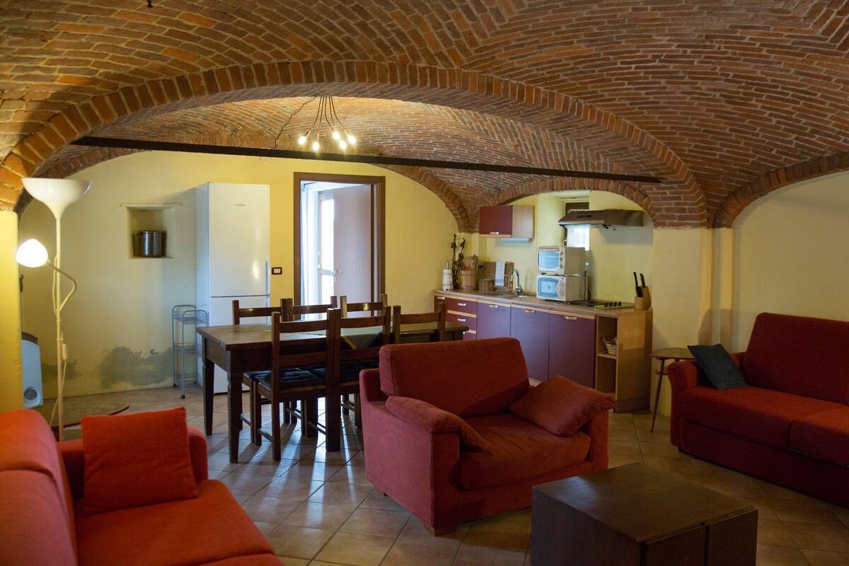 Una sala de estar acogedora con sofás rojos, una mesa de comedor y una zona de cocina con techo de ladrillo.