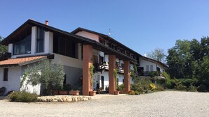 A two-story building with a balcony, a gravel driveway, and surrounding greenery. - Agriturismo & Scuderia Fano's Farm (Suno)