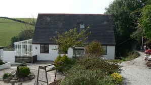 A small, single-story house with a sloped roof, a conservatory, and a gravel driveway.