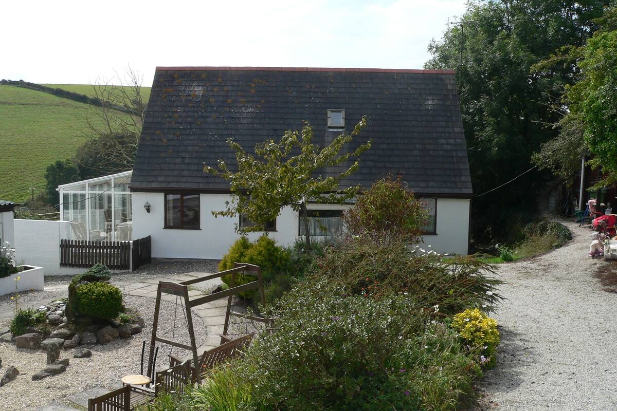 A small, single-story house with a sloped roof, a conservatory, and a gravel driveway.
