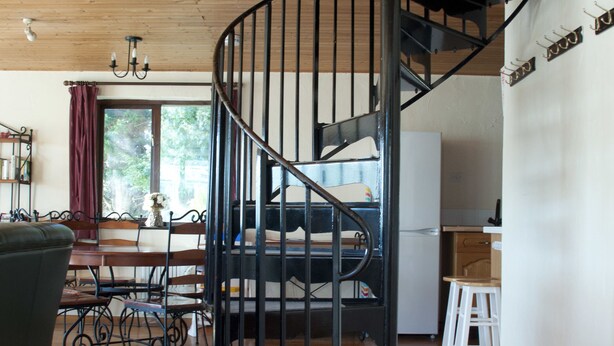 A spiral staircase in a wooden interior with a dining area and kitchen in the background.