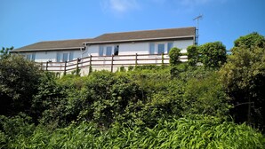 A two-story house with a sloped roof, surrounded by dense greenery.