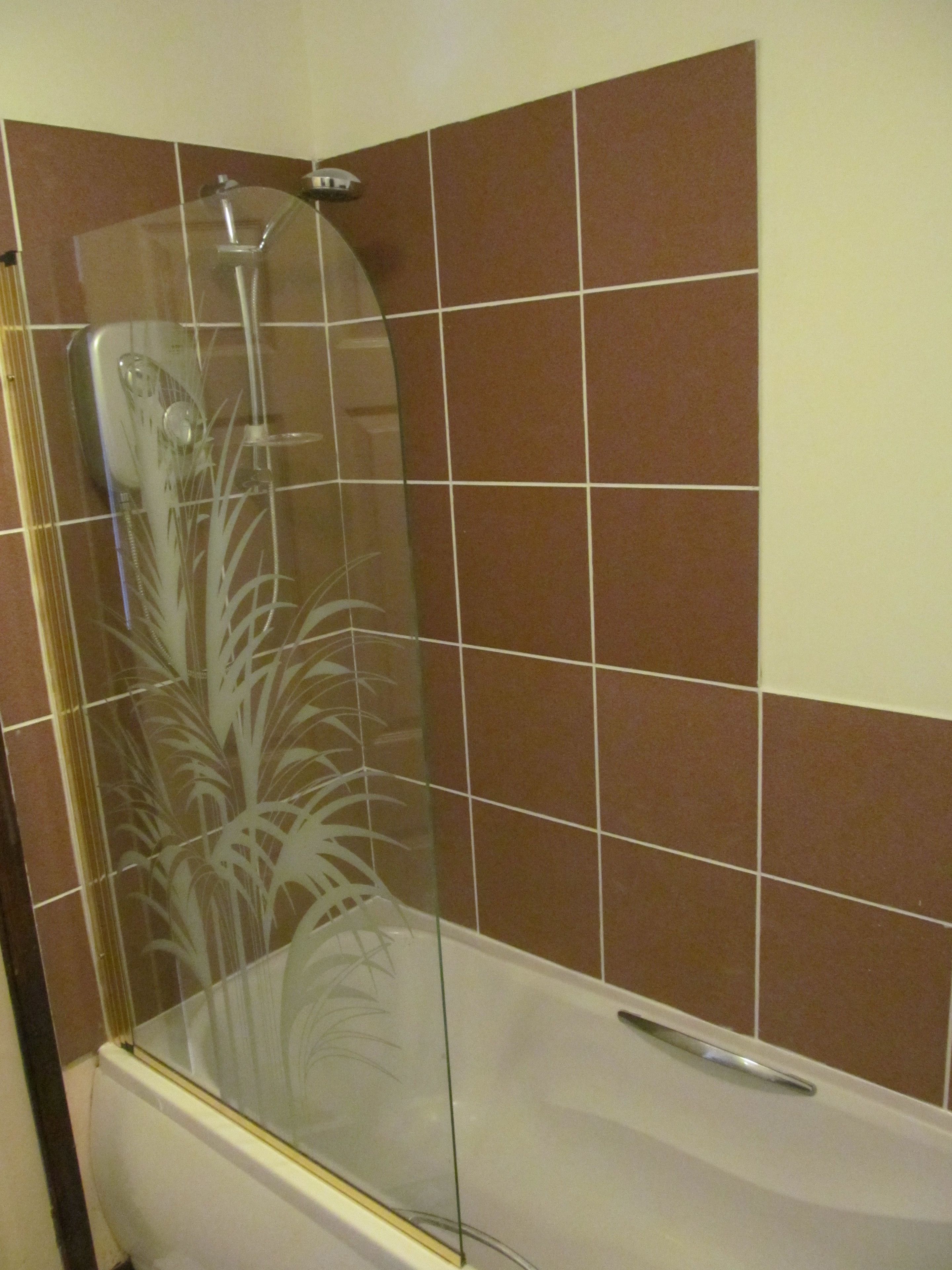 A bathroom with a glass-enclosed shower, a white bathtub, and brown tiled walls.