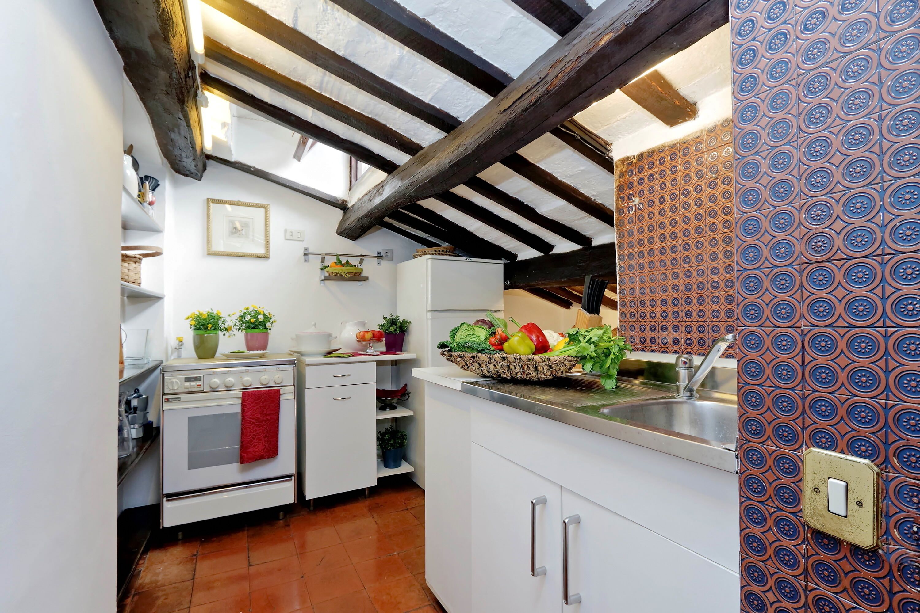 A compact kitchen with a white stove, a red towel hanging on it, and a sink with a patterned backsplash.