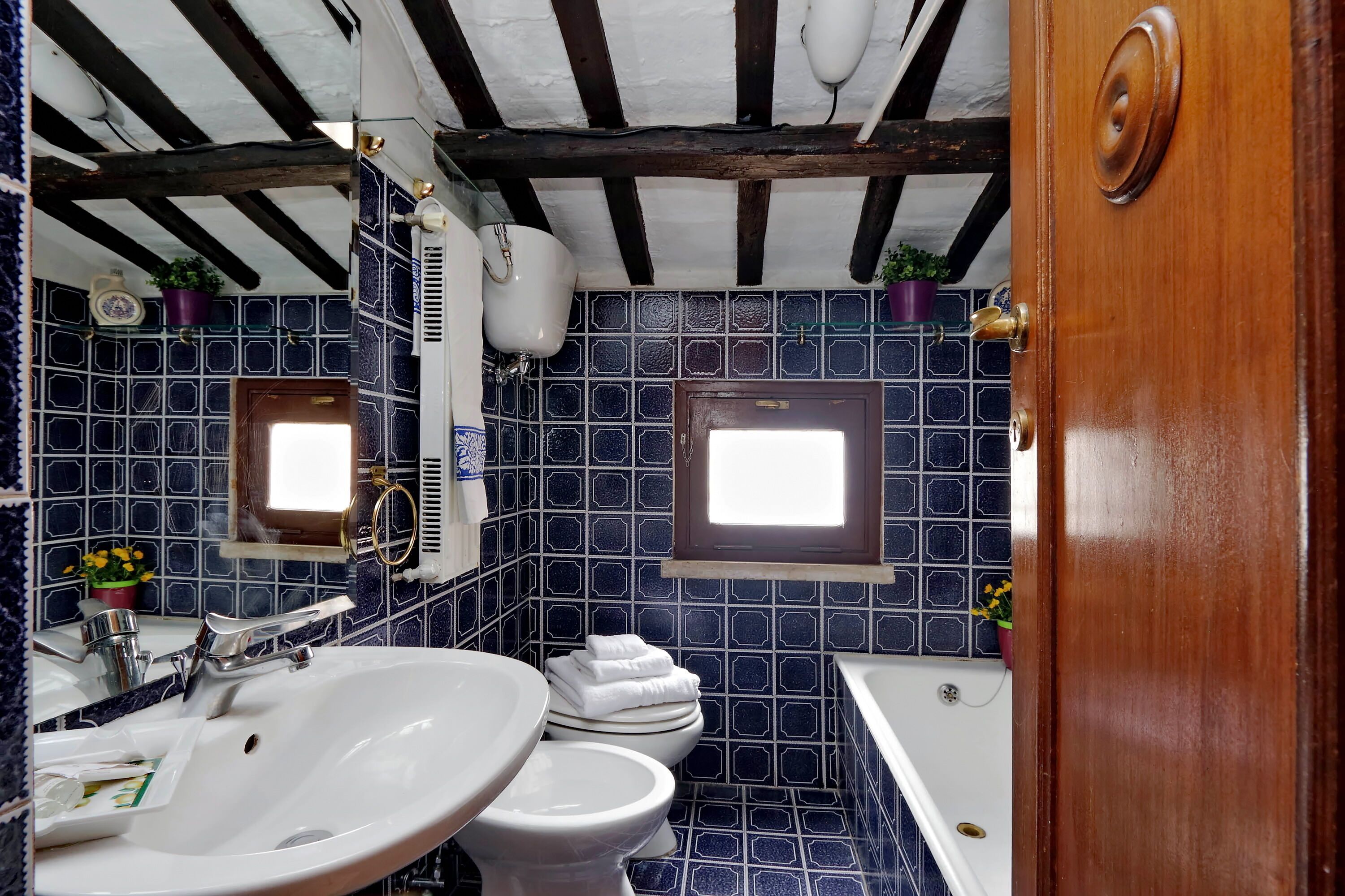 A bathroom with a white sink, a toilet, and a bathtub. There are blue tiles on the walls and a wooden ceiling.