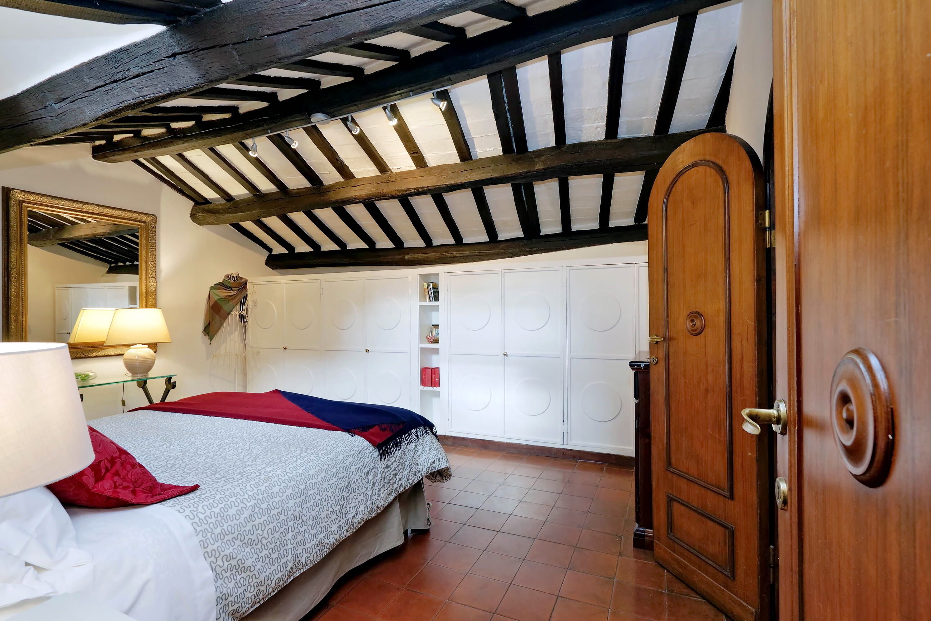 Un dormitorio con una cama, una puerta de madera, un armario y un espejo.