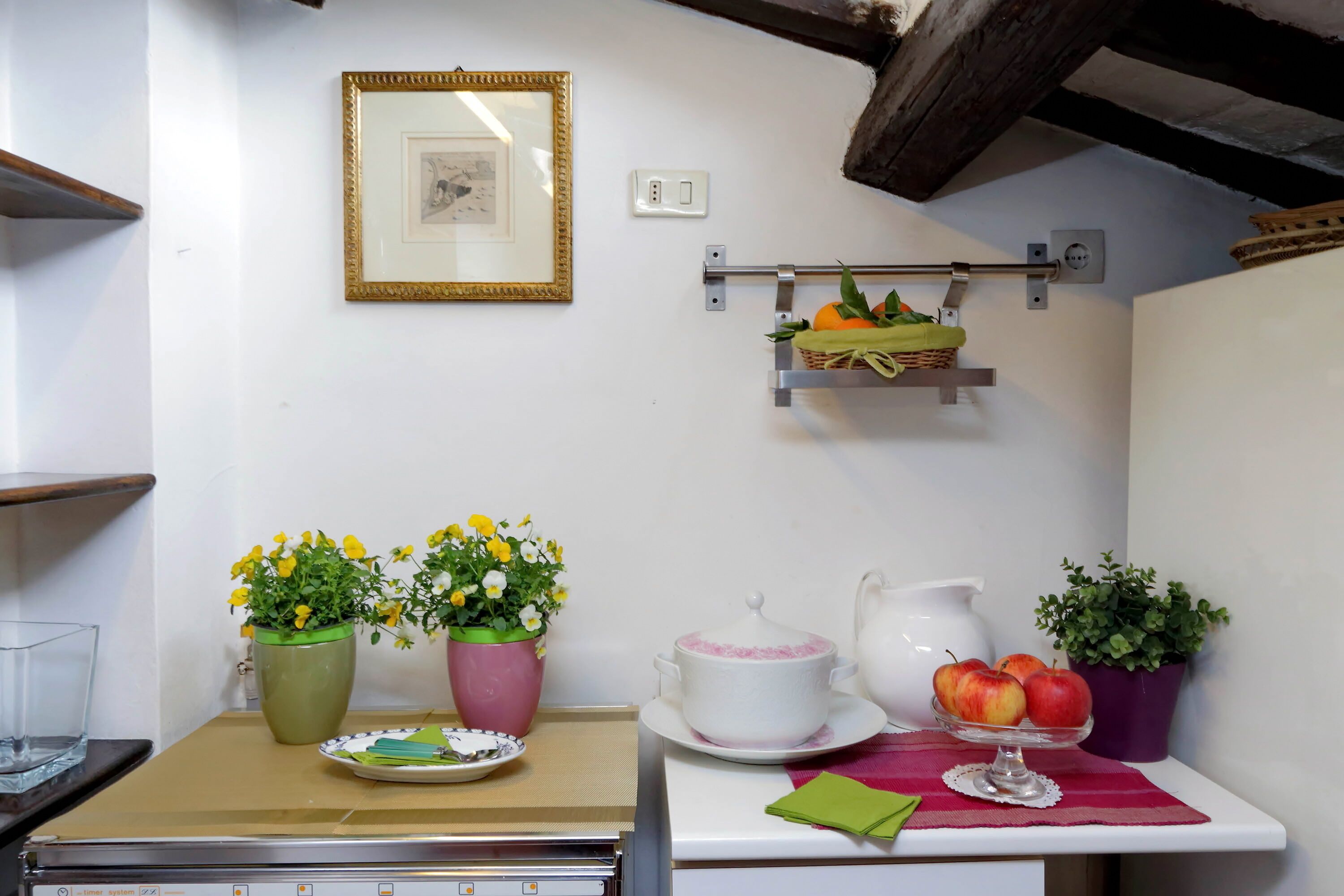 A kitchen with a countertop, a sink, a cabinet, and a wall-mounted shelf with a basket of fruits and vegetables.