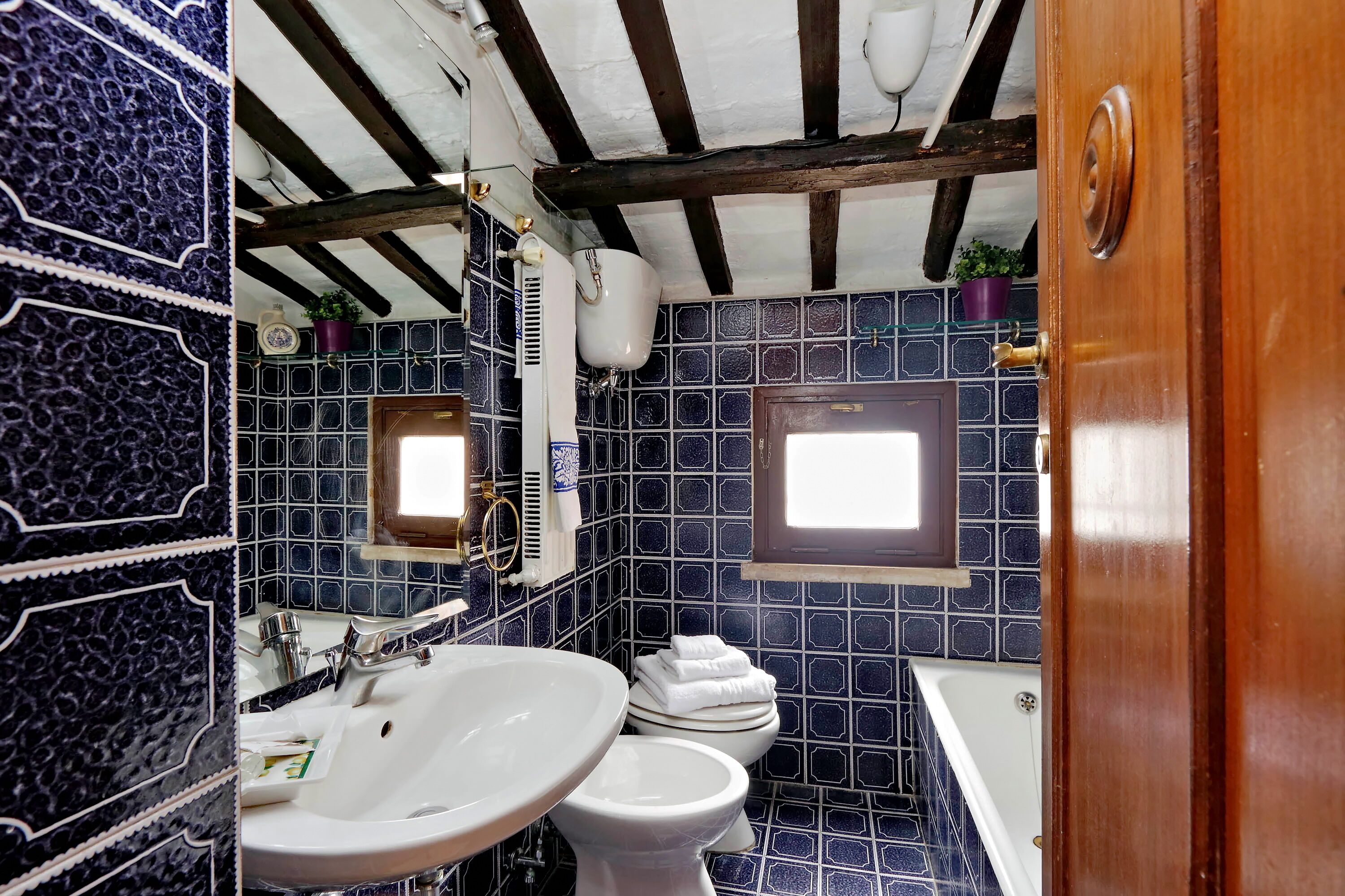 A bathroom with a white sink, a toilet, and a bathtub. The walls are tiled in a blue pattern.