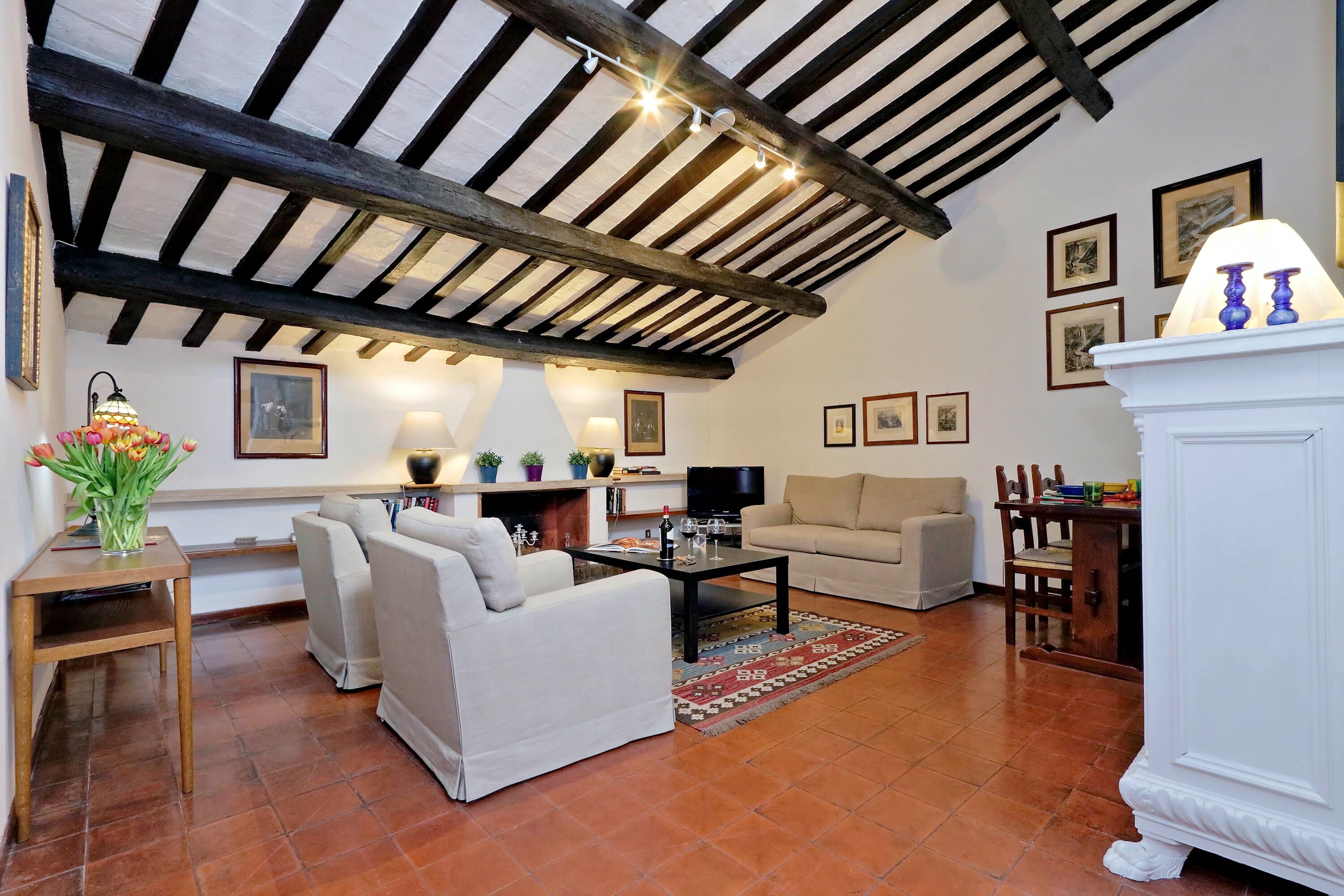 A cozy living room with a high ceiling, a fireplace, a sofa, a coffee table, and a dining area with chairs.