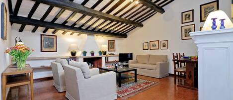 A cozy living room with a high ceiling, a fireplace, a sofa, a coffee table, and a dining area with chairs.