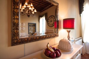 Una stanza con un grande specchio, un lampadario, un orologio e una ciotola di frutta su un comò.