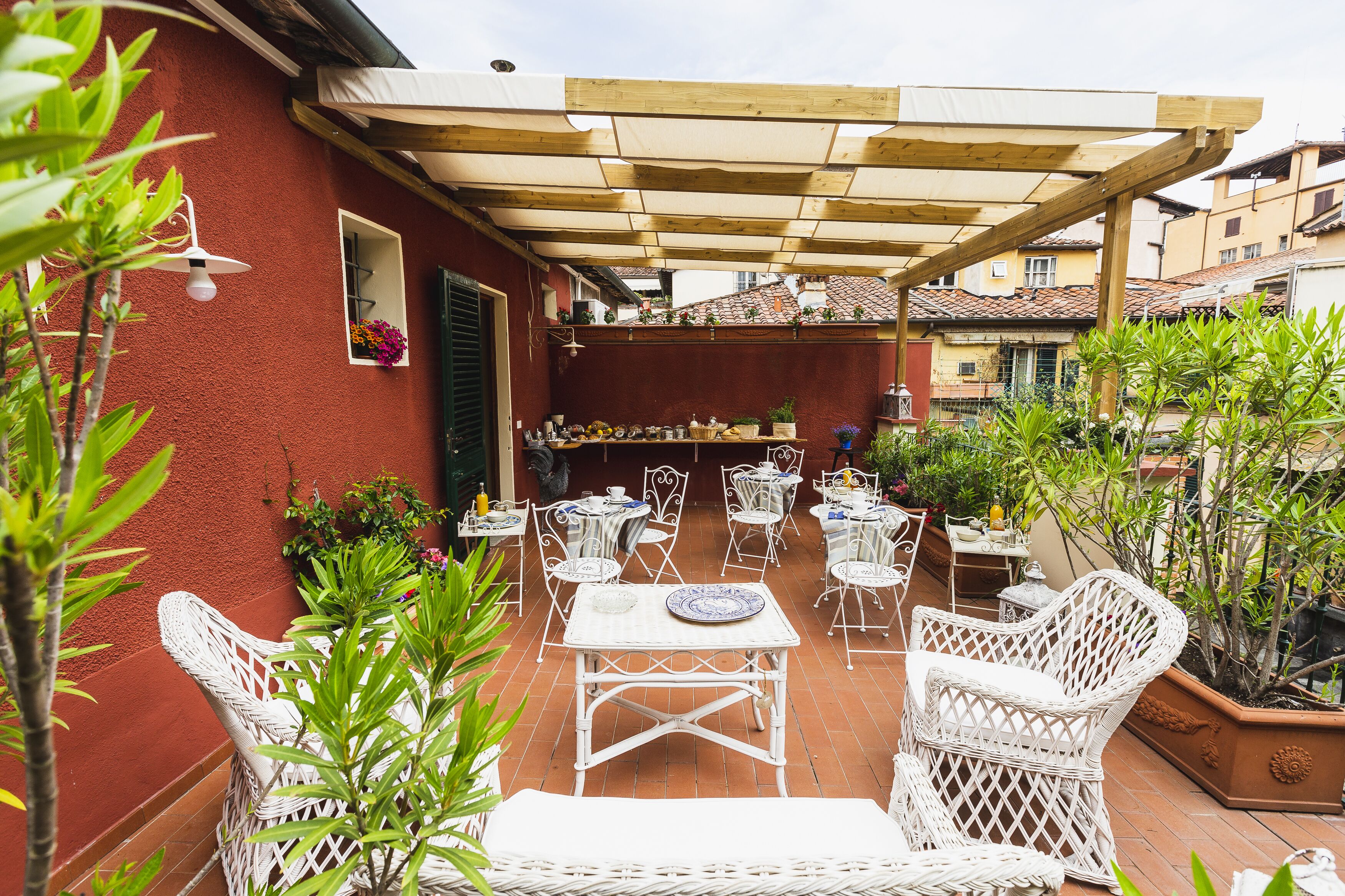 An outdoor patio with white wicker furniture, a wooden pergola, and potted plants.