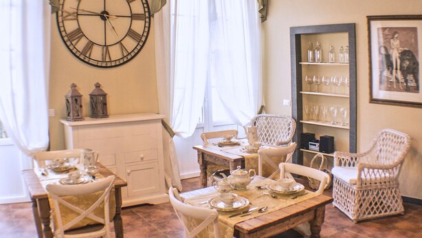 Un comedor con candelabro, un reloj de pared grande y sillas de mimbre.