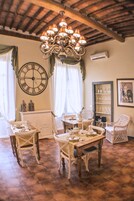 Zona pranzo con un lampadario, un orologio da parete grande e sedie in vimini.