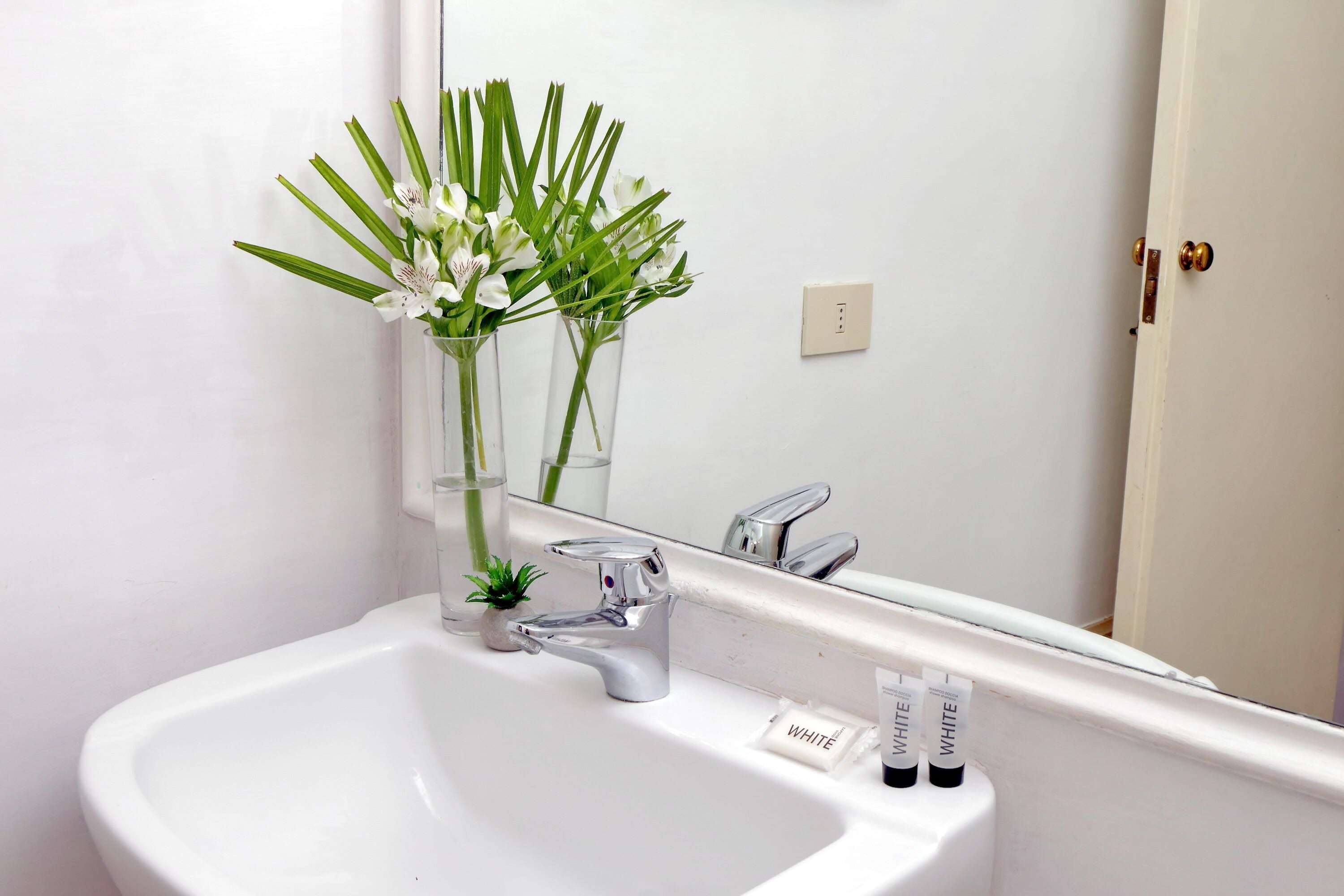A bathroom with a white sink, a mirror, and a vase with flowers.