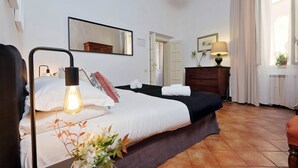 Un dormitorio con cama, lámpara de noche, espejo, cómoda y ventana con cortinas.