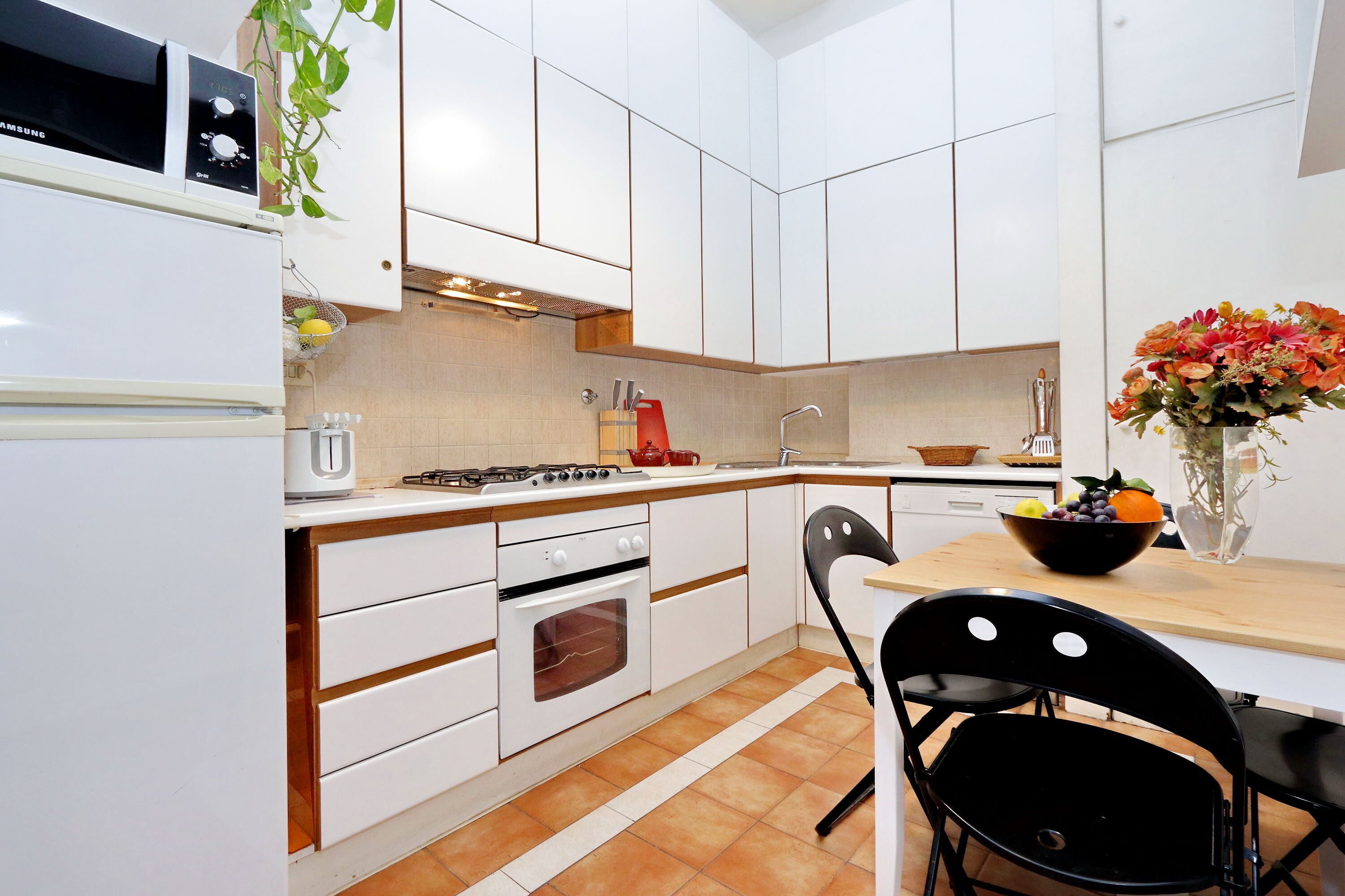 A modern kitchen with white cabinets, a built-in oven, a microwave, and a dining area with a table and chairs.