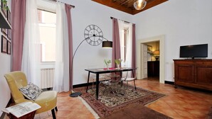 Una sala de estar con un sillón amarillo, una mesa de comedor con sillas, un reloj en la pared, un televisor y un mueble de madera.