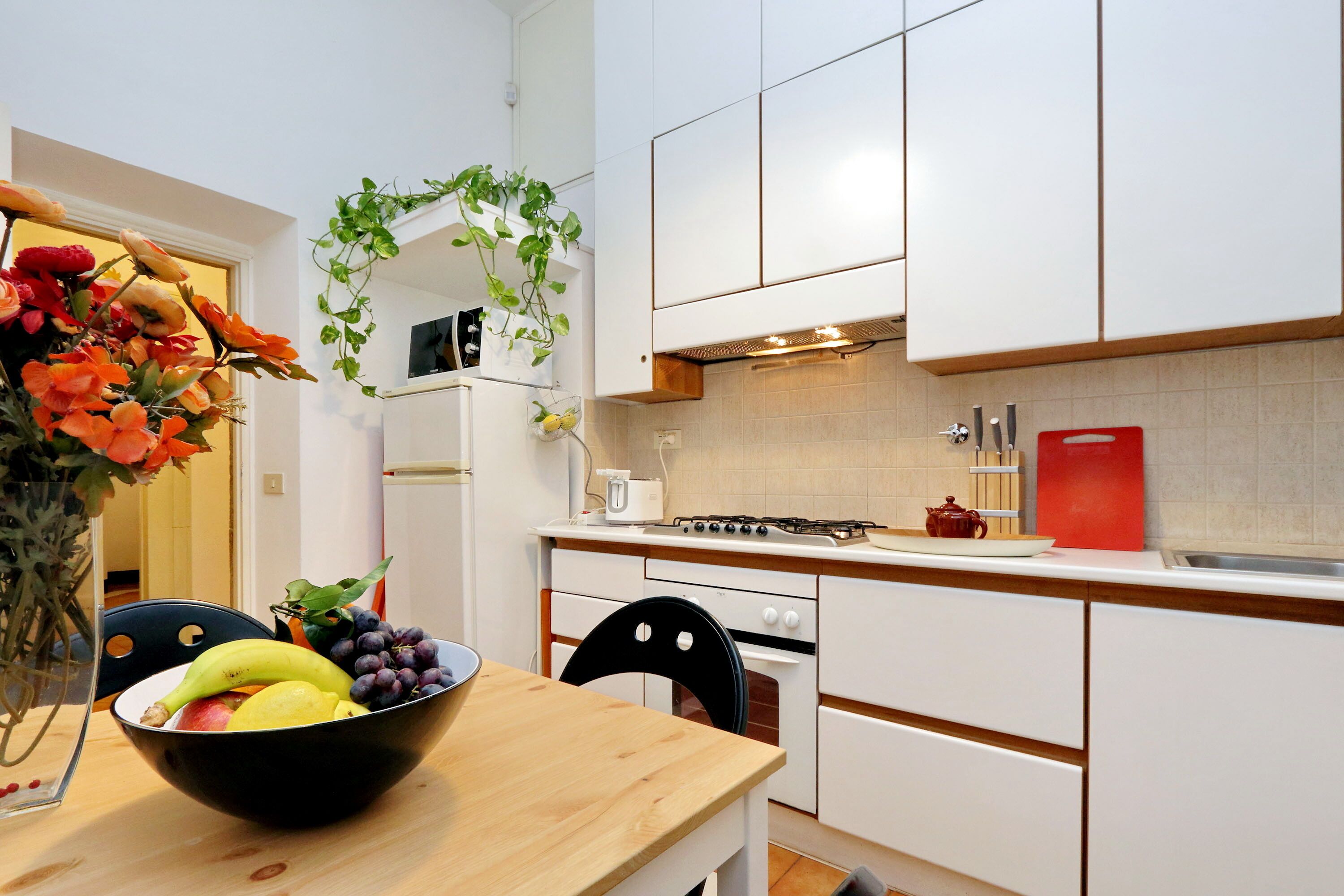 Une cuisine moderne avec des meubles blancs, un plan de travail en bois et une table à manger agrémentée d’un panier de fruits.