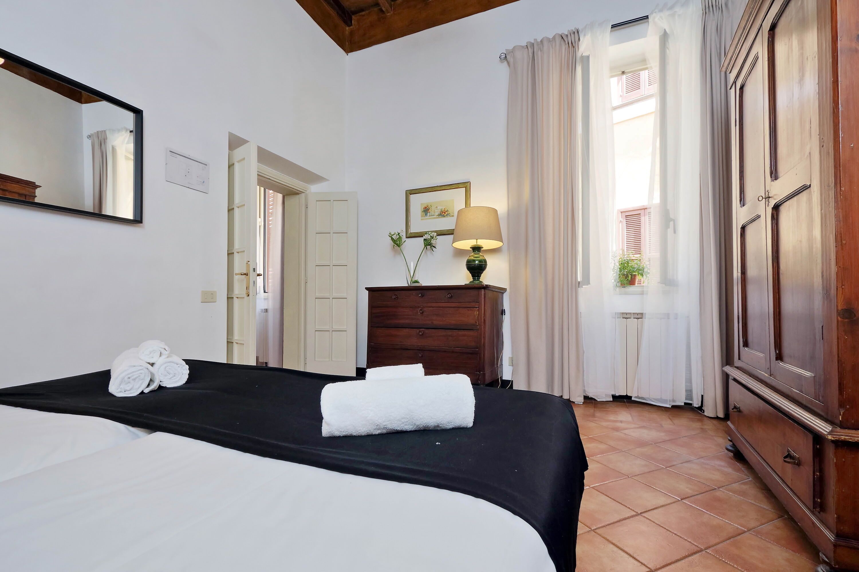 A hotel room with a bed, a dresser, a lamp, and a window with curtains.