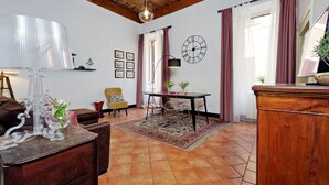 Una sala de estar acogedora con techo de madera, una mesa de comedor con sillas, un sofá, una lámpara y un reloj en la pared.