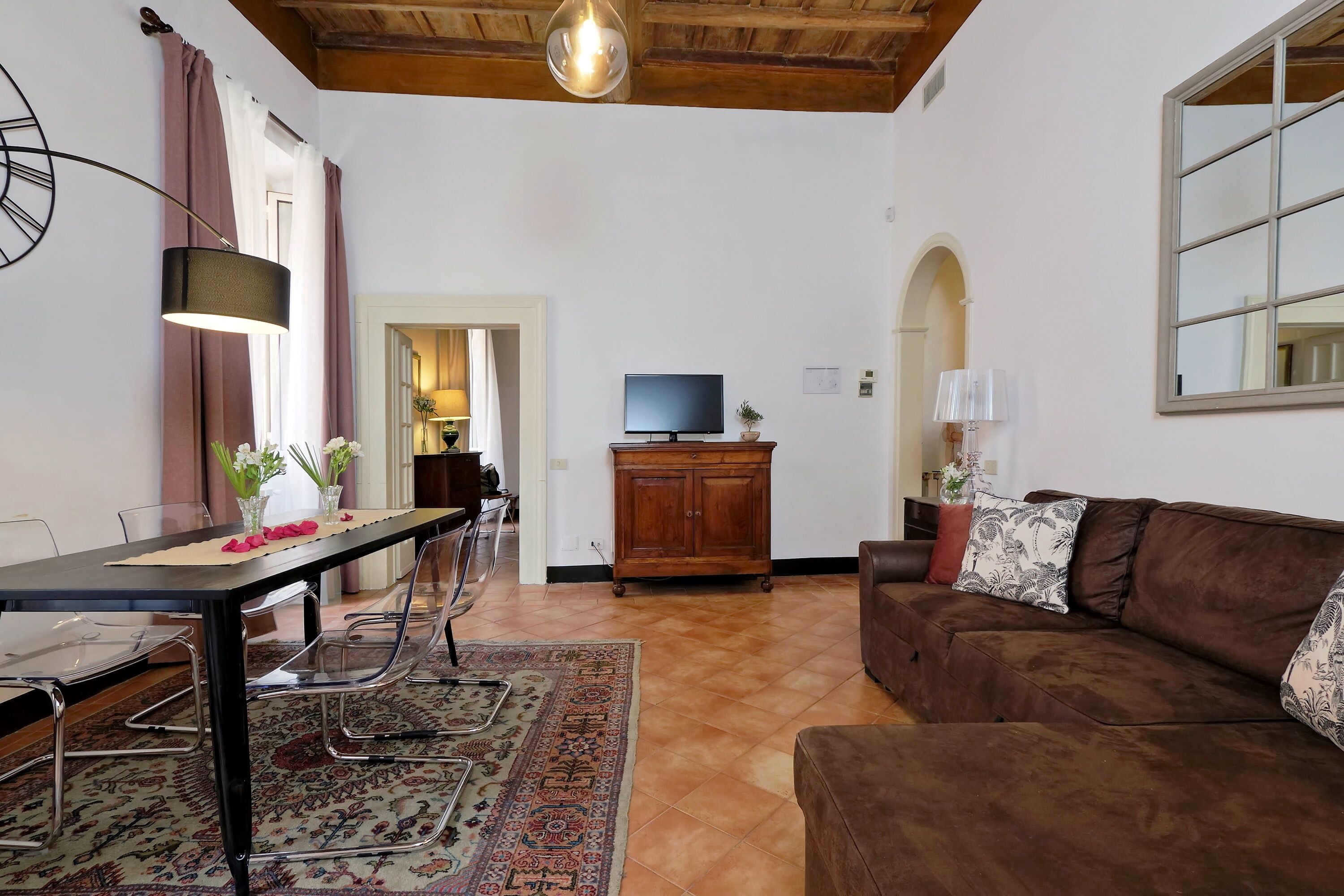 A living room with a brown sofa, a dining table with chairs, a TV, and a wooden cabinet.