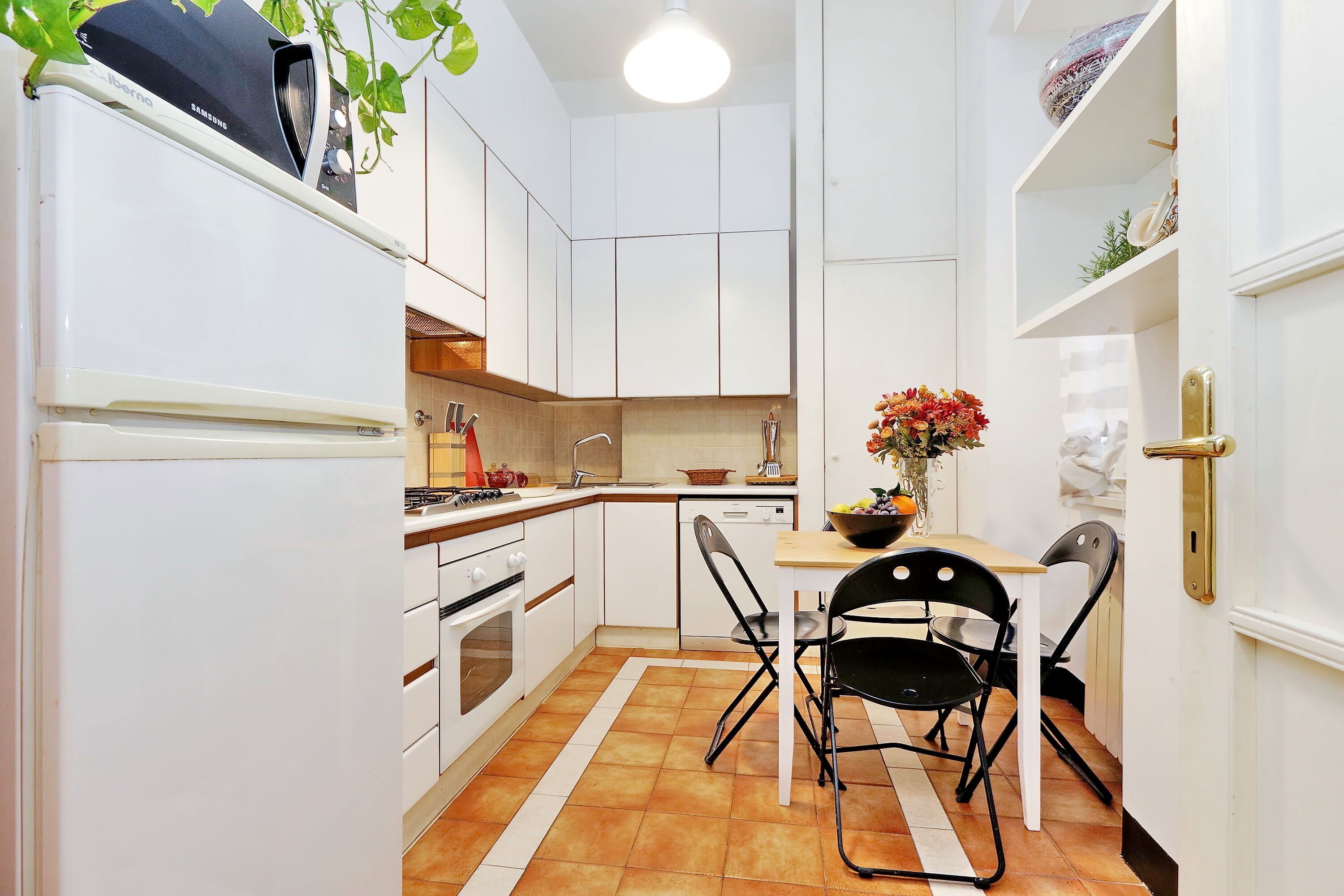 Een compacte keuken met witte kasten, een inbouwoven, een spoelbak en een eethoek met een tafel en stoelen.