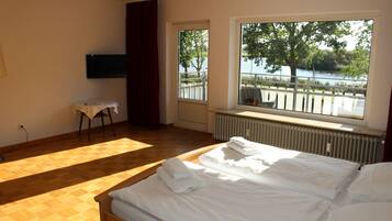 Habitación de hotel con cama, una mesita, televisor y ventana con vistas al agua y árboles.