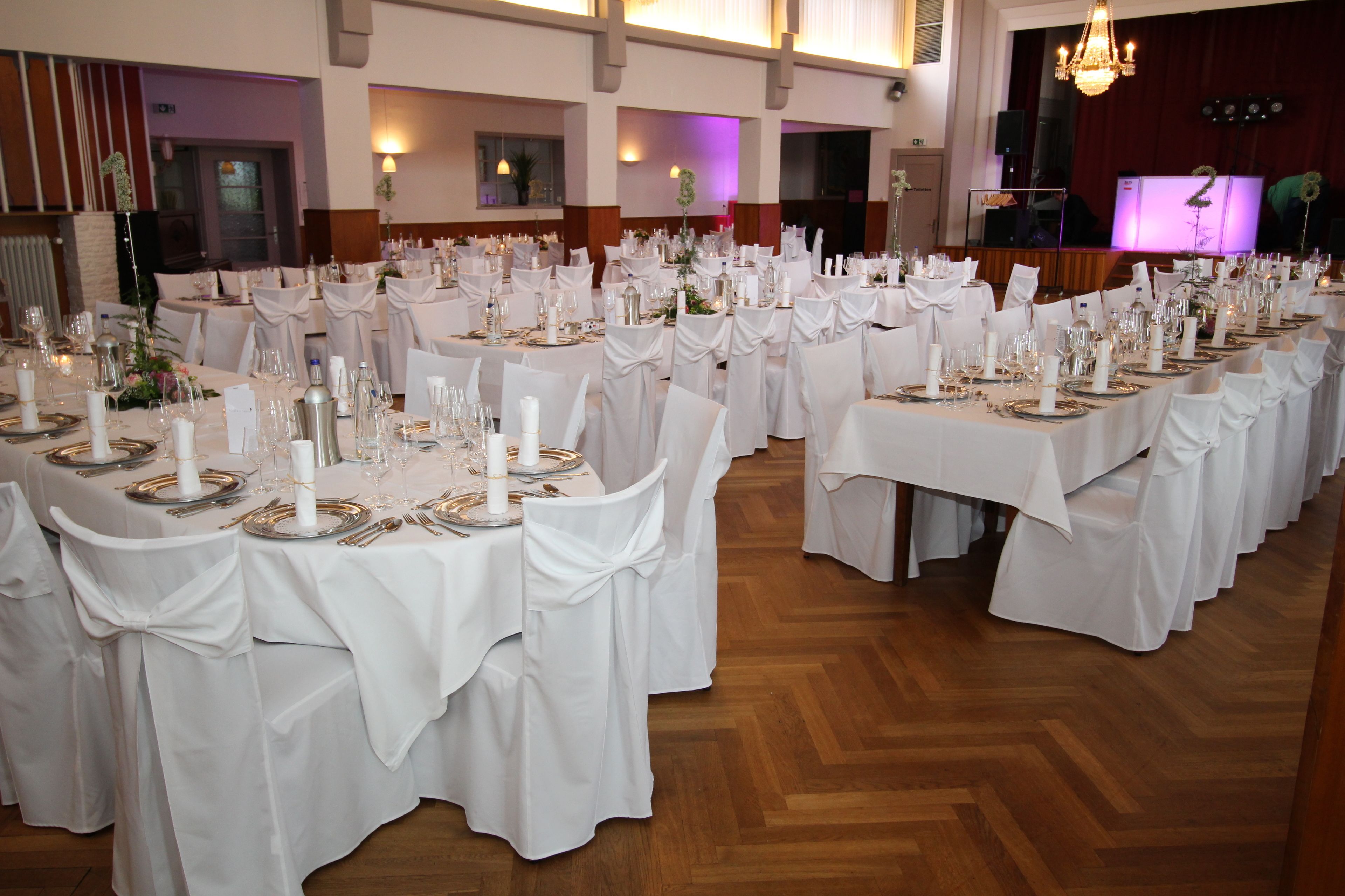 Un salón de banquetes con varias mesas redondas preparadas para un evento formal, con manteles blancos, sillas y elegantes centros de mesa.