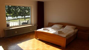 A bedroom with a wooden bed, a window with a view of trees and a body of water, and a radiator under the window.