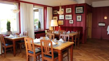 A dining area with wooden tables and chairs, a chandelier, and framed pictures on the walls.