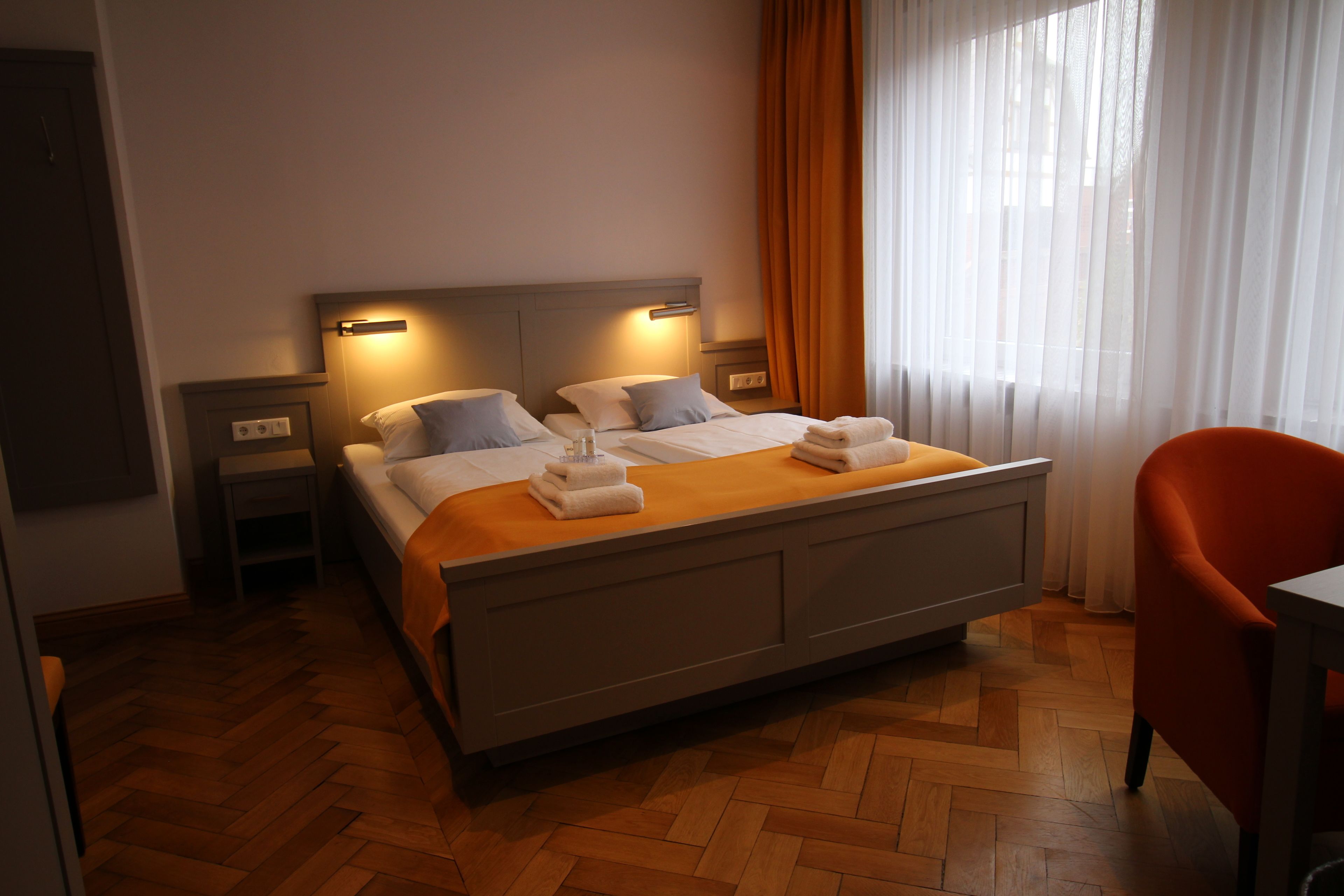 A hotel room with a large bed, two bedside tables, a chair, and a window with curtains.