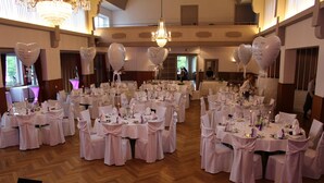 A banquet hall with round tables set for a formal event, featuring white tablecloths, chairs with sashes, and heart-shaped balloons. - Hotel Zur Treene (Schwabstedt)